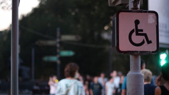 Sign of a Disabled Person Sitting on a Wheelchair Against the Background of Blurred Walking People