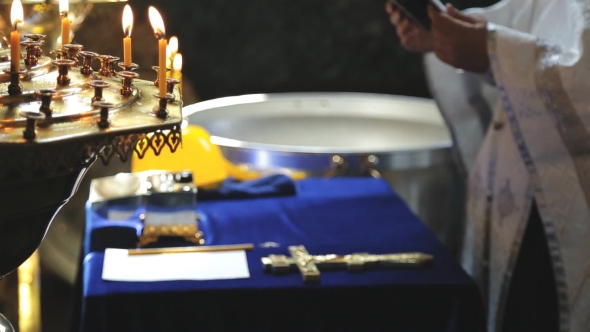 Priest in a Cassock Holds a Bible, Stands Before the Cross and Reads a Prayer at a Rite of Baptism. alt