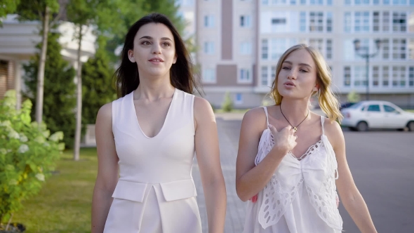 Two Charming Girls in White Stylish Dresses Talking Lively on Background of Street in Summer alt