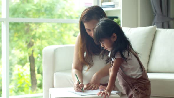 Young mother drawing on paper while teaching her daughter