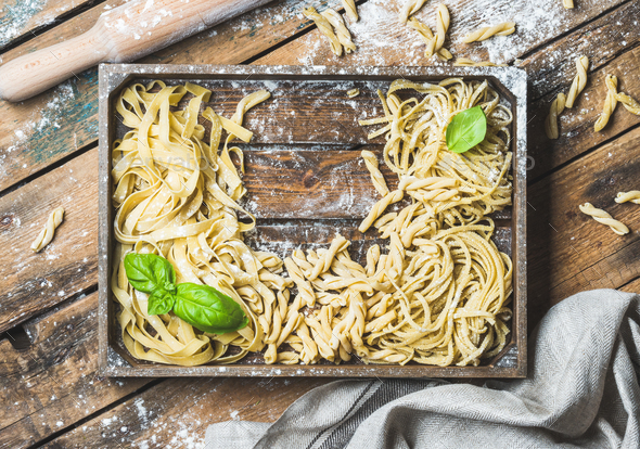 Various uncooked Italian pasta in wooden tray with basil leaves - Stock Photo - Images