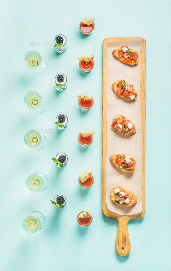 Snacks, brushettas, gazpacho shots, desserts, champagne over pastel blue background - Stock Photo - Images