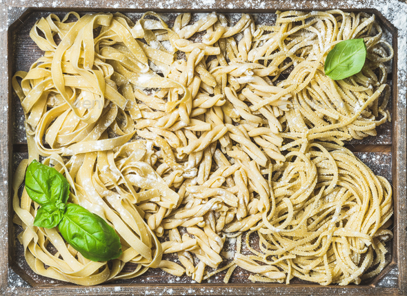Uncooked Italian pasta in wooden tray with basil and flour - Stock Photo - Images