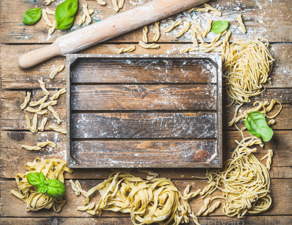 Various homemade uncooked Italian pasta and wooden tray in center - Stock Photo - Images