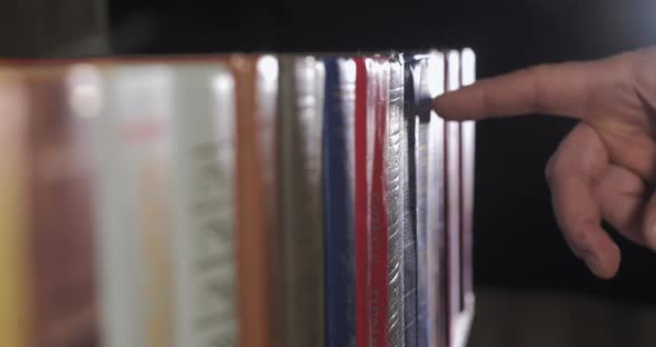 A Mans Hand is Looking for the Right Book Among a Collection of Volumes alt