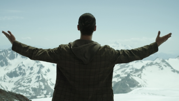 Young Bearded Man Spreads Arms at Snowy Mountains with Scenic View