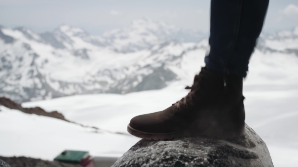 Hiker Feet in Leather Boot Stomps on Stone at Snowy Mountain Scenic View