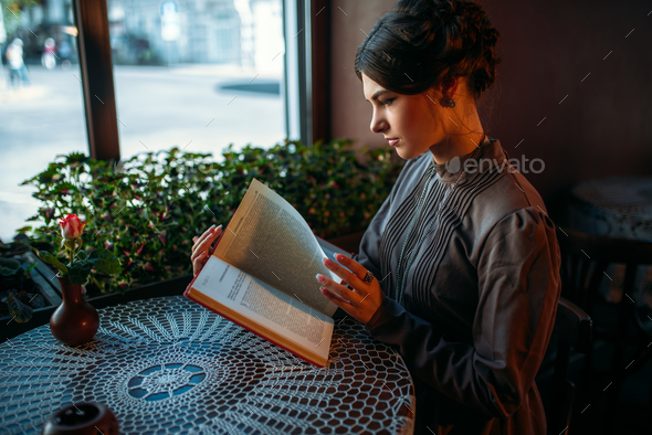 Portrait of lady in cafe reading book near window - Stock Photo - Images