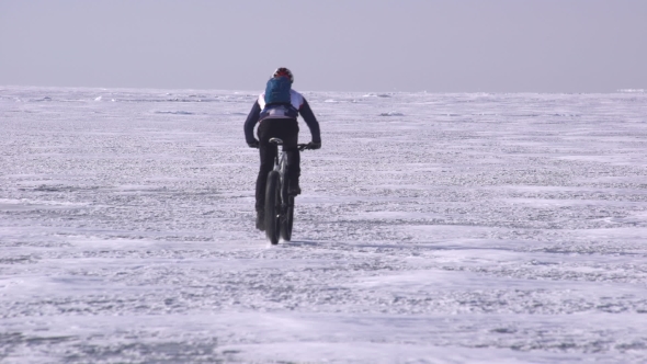 a Sportive Man Riding a Bicycle Across a Frozen Lake