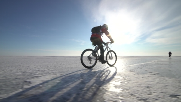a Man Riding a Bicycle Across a Frozen Lake alt