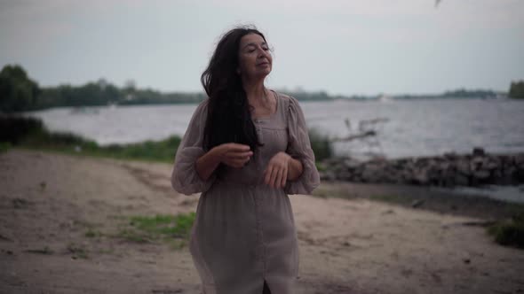 Portrait of Calm Confident Senior Woman Walking on Lake Shore at Dusk Looking Away alt