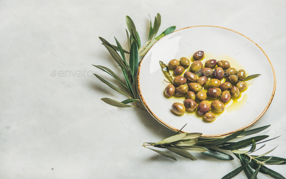 Pickled green Mediterranean olives in oil and olive tree branch - Stock Photo - Images