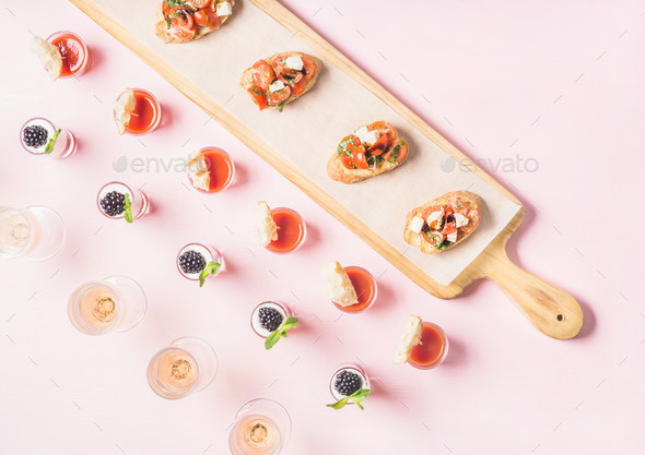 Snacks, brushetta sandwiches, gazpacho shots, desserts over pastel pink background - Stock Photo - Images