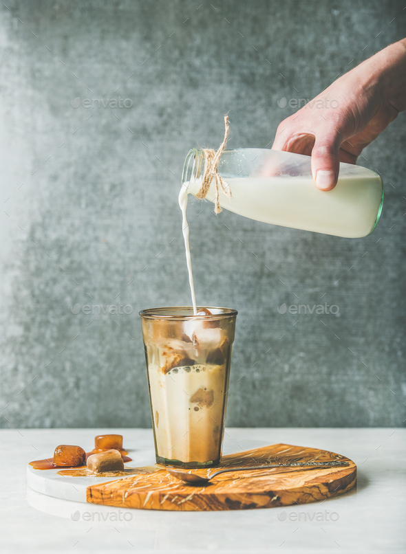 Man's hand pouring milk to Iced latte caramel coffee cocktail - Stock Photo - Images