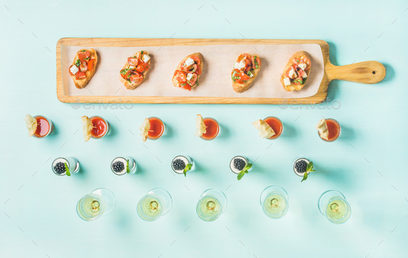 Snacks, brushettas, gazpacho shots, desserts, champagne over pastel blue background - Stock Photo - Images