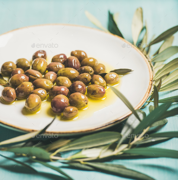 Pickled olives on plate and olive-tree branch over blue background - Stock Photo - Images
