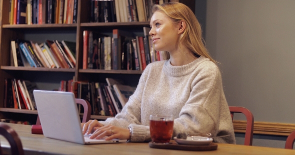 Woman in Jumper Using Laptop in Library alt