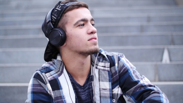Young Trendy Man Listen To Music on Smartphone Sitting on the Steps Outdoor