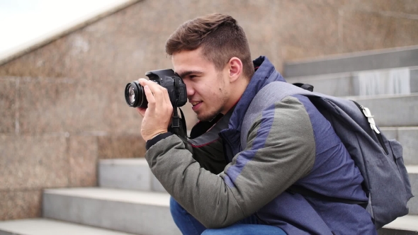 Young Handsome Man Takes Photo of the Camera with Own Camera and Smiles