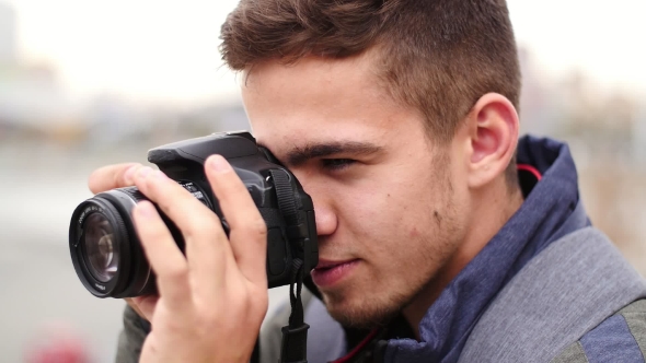 Young Handsome Man Takes Photo of the Camera with Own Camera and Smiles