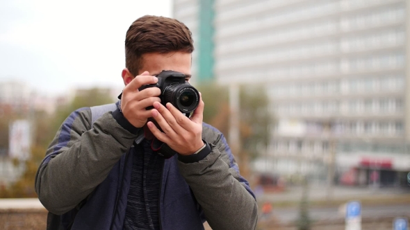 Young Handsome Man Takes Photo of the Camera with Own Camera and Smiles