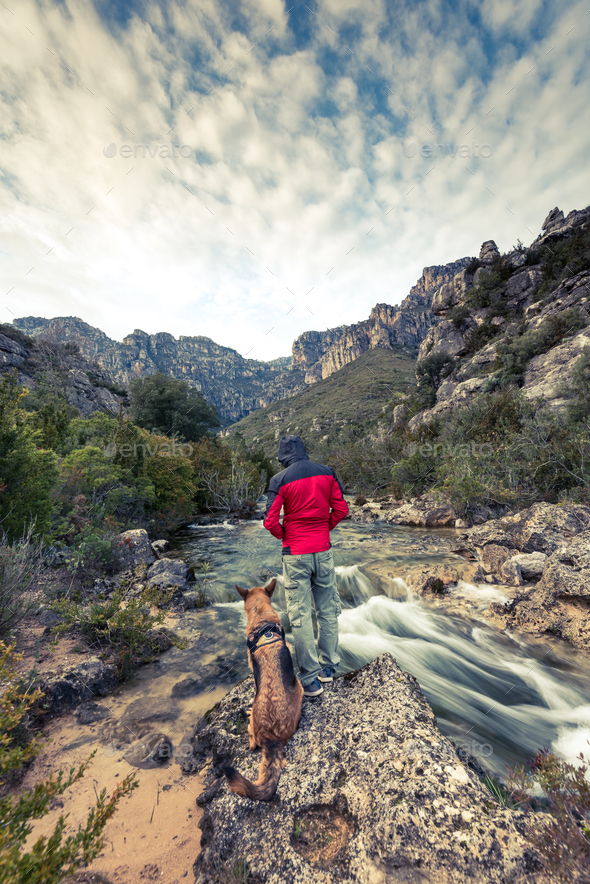 Wanderlust man and dog in wild mountains by the river
