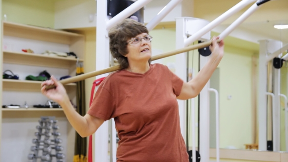 Elderly Woman Swinging with Stick, Doing Physiotherapy Exercises in Fitness Room. Healthy Gymnastics