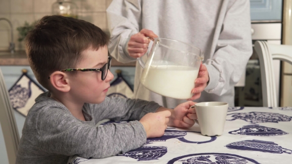 Mother Pouring Milk into a Cup and Gives Drink to his Child alt