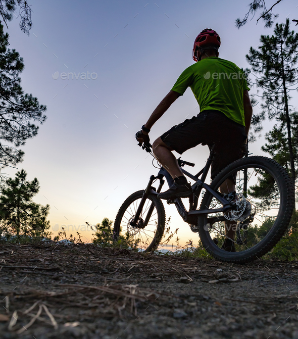Mountain biker looking at sunset, bike trail in autumn mountains