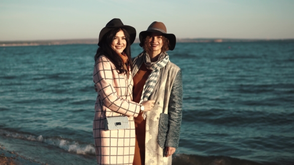 Two Cute Young Women Are Smiling and Enjoying Life on an Autumn Walk Along the Ocean