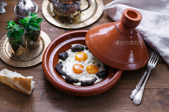 Fried eggs and beef in tajine dish with cover, Moroccan breakfast