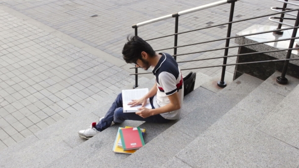 Happy Male Asian Student Sitting on Stairs and Reading Book