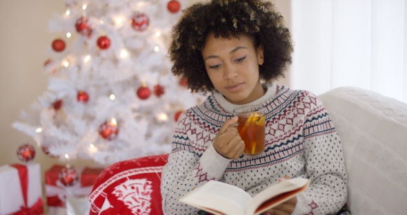 Woman Reading a Book in Front of a Christmas Tree