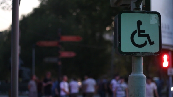 Sign of a Disabled Person Sitting on a Wheelchair Against the Background of Blurred Walking People