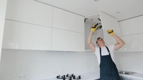  Carpenter repair and assembling cabinet at the modern kitchen of white color. Furniture installing alt