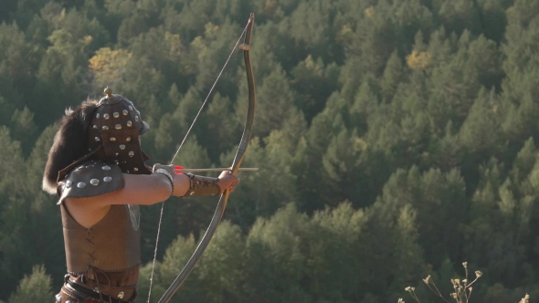 Archer in Th Armor Releases Arrow Into Dense Forest in Summer.