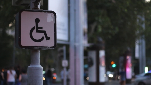 Sign of a Disabled Person Sitting on a Wheelchair Against the Background of Blurred Walking People