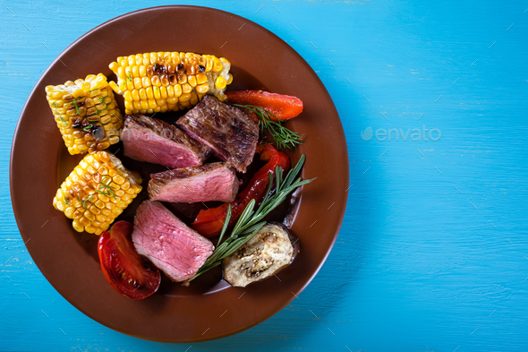 Slices of fried meat with corn and vegetables on plate - Stock Photo - Images