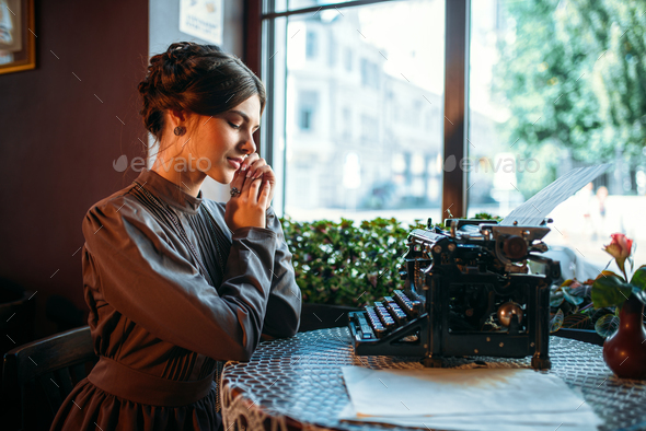 Smiling lady sits by table with ancient typewriter - Stock Photo - Images