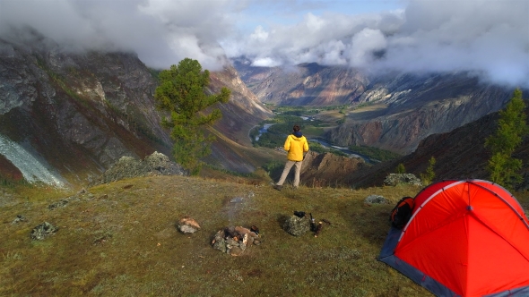 Aerial Footage of a Man Standing Near a Tent in Front of Mountain Valley.