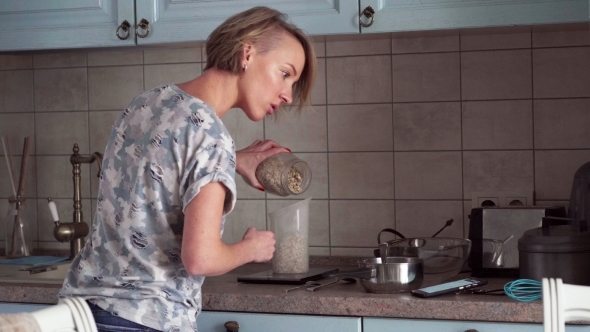 Woman Prepares a Food and Looks on Smartphone Screen
