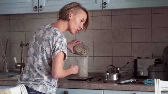 Woman Prepares a Food and Looks on Smartphone alt