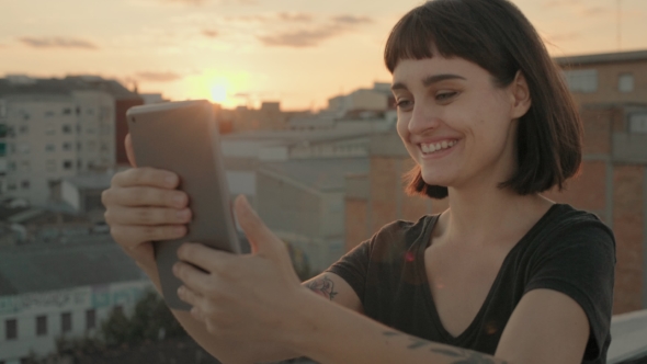 Attractive Brunette with Gadget on Rooftop at Sunset