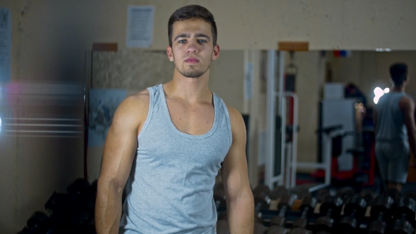 In the Gym, a Man Looks in the Mirror and Makes Swings with Muscular Arms