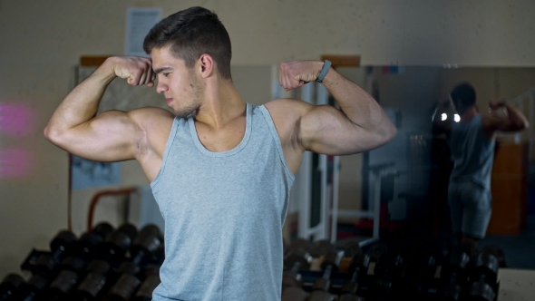 In the Gym, a Man Looks in the Mirror and Makes Swings with Muscular Arms