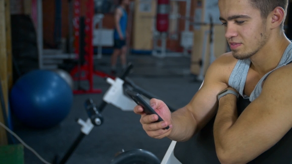 Athletic Man Sitting in Fitness Gym After Workout, Chatting Online Smart Phone