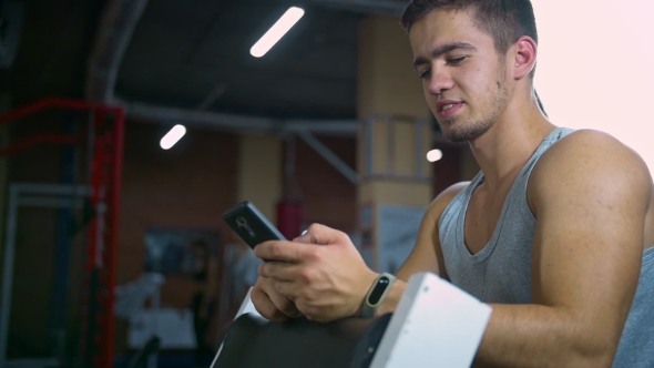 Athletic Man Sitting in Fitness Gym After Workout, Chatting Online Smart Phone