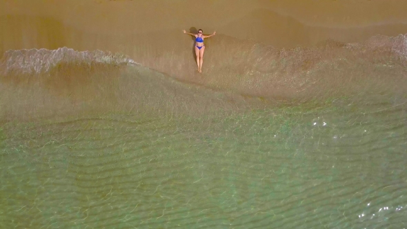 Woman in a Bikini Lying on a Sandy Beach and Waves Wash Her Feet alt