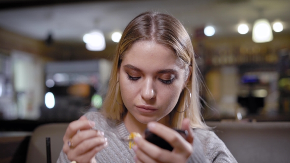 Young Woman Is Eating Dessert at a Table in Coffee House and Watching Videos alt