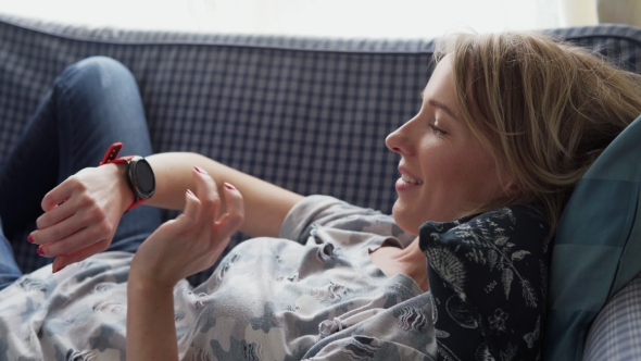 Happy Adult Woman Using Smart Watch on Sofa at Home